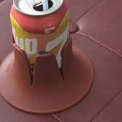 A burgundy drink base holding a red-and-yellow caffeine-free soda can with a blue straw, sitting on a tufted burgundy leather ottoman